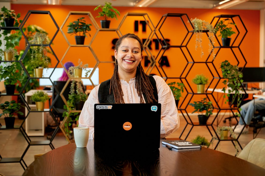 IT professional zit achter haar laptop en lacht in de camera.