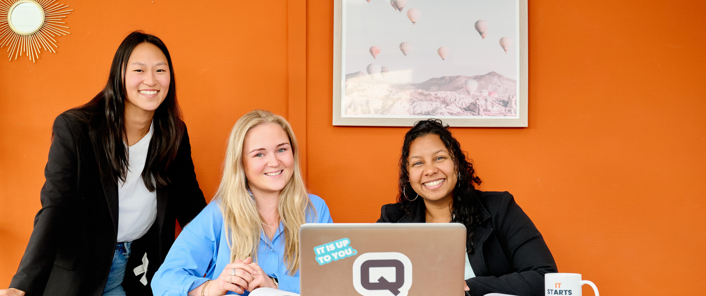 vrouwelijke IT-professionals van QISS IT zitten aan tafel met een laptop en lachen